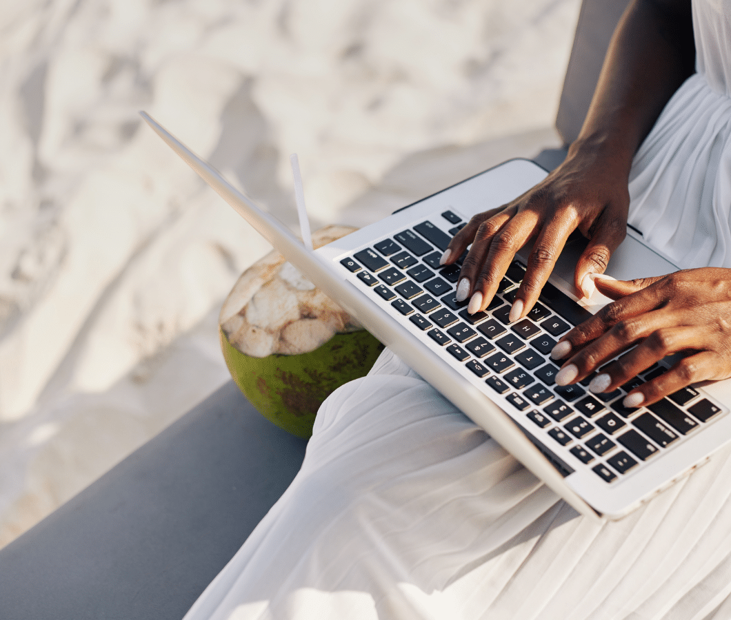 Woman working on her laptop on the beach | 6 Tips to Keep Your Marketing Powerful During Holiday Season